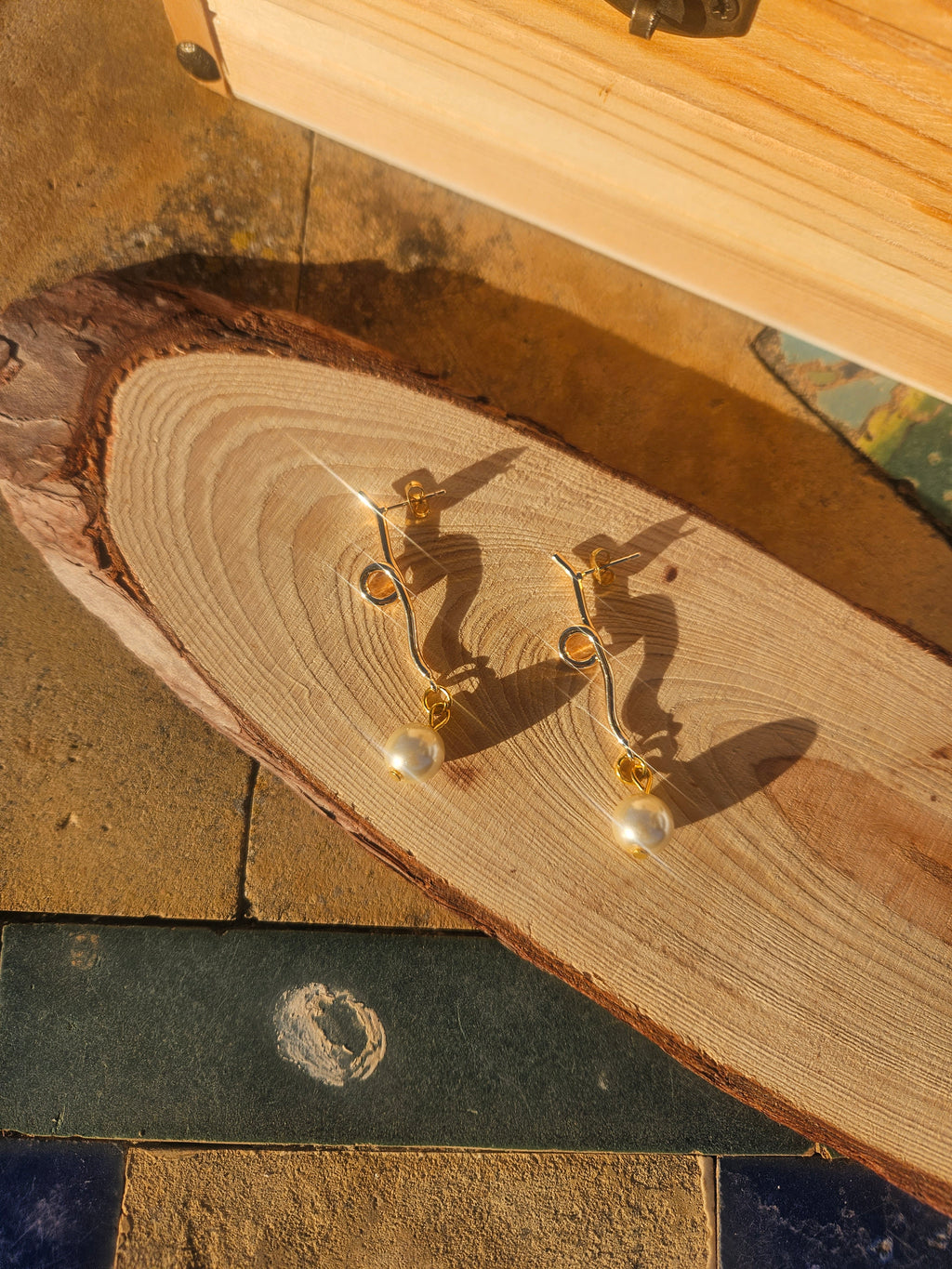 Pendientes dorados colgantes con perla, sobre tablón de madera rústica