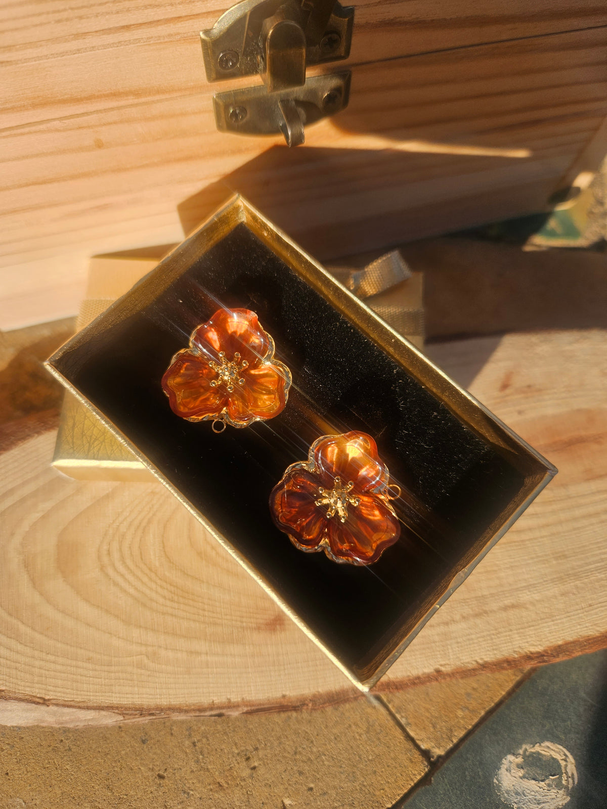 Pendientes flor ámbar en caja: motivo central brillante con marco dorado y cierre visible.