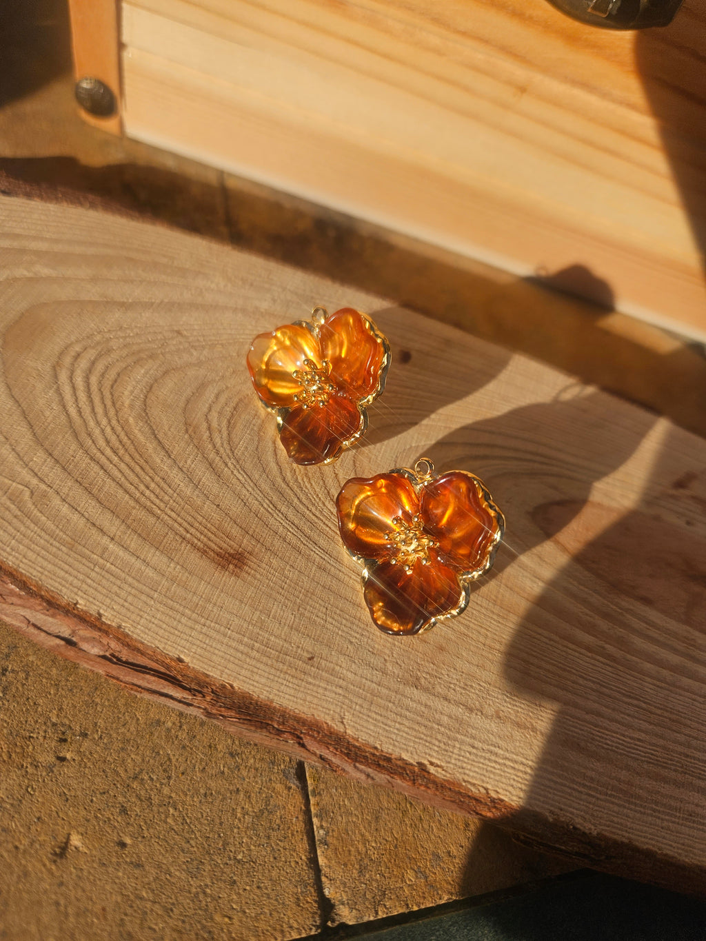 Pendientes flor ámbar con brillo central y contorno dorado, vistos sobre superficie de madera.