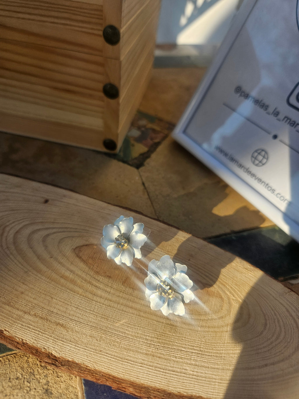 Pendientes de flor azul con centro dorado, sobre soporte blanco y madera.