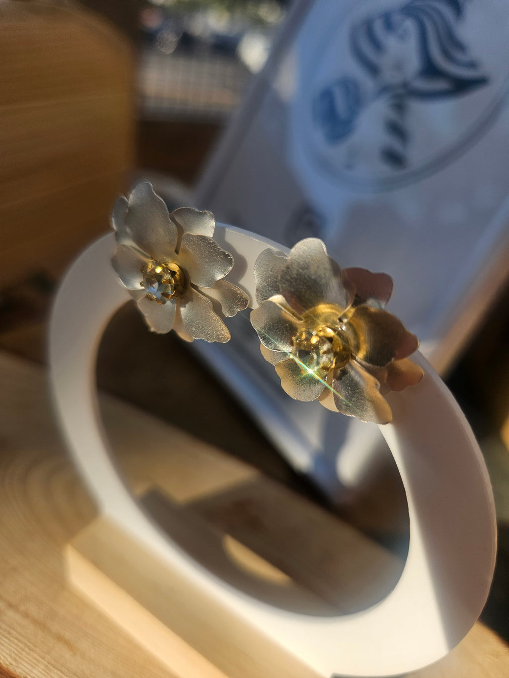 Pendientes de flor azul con centros dorados, par sobre aro circular blanco.