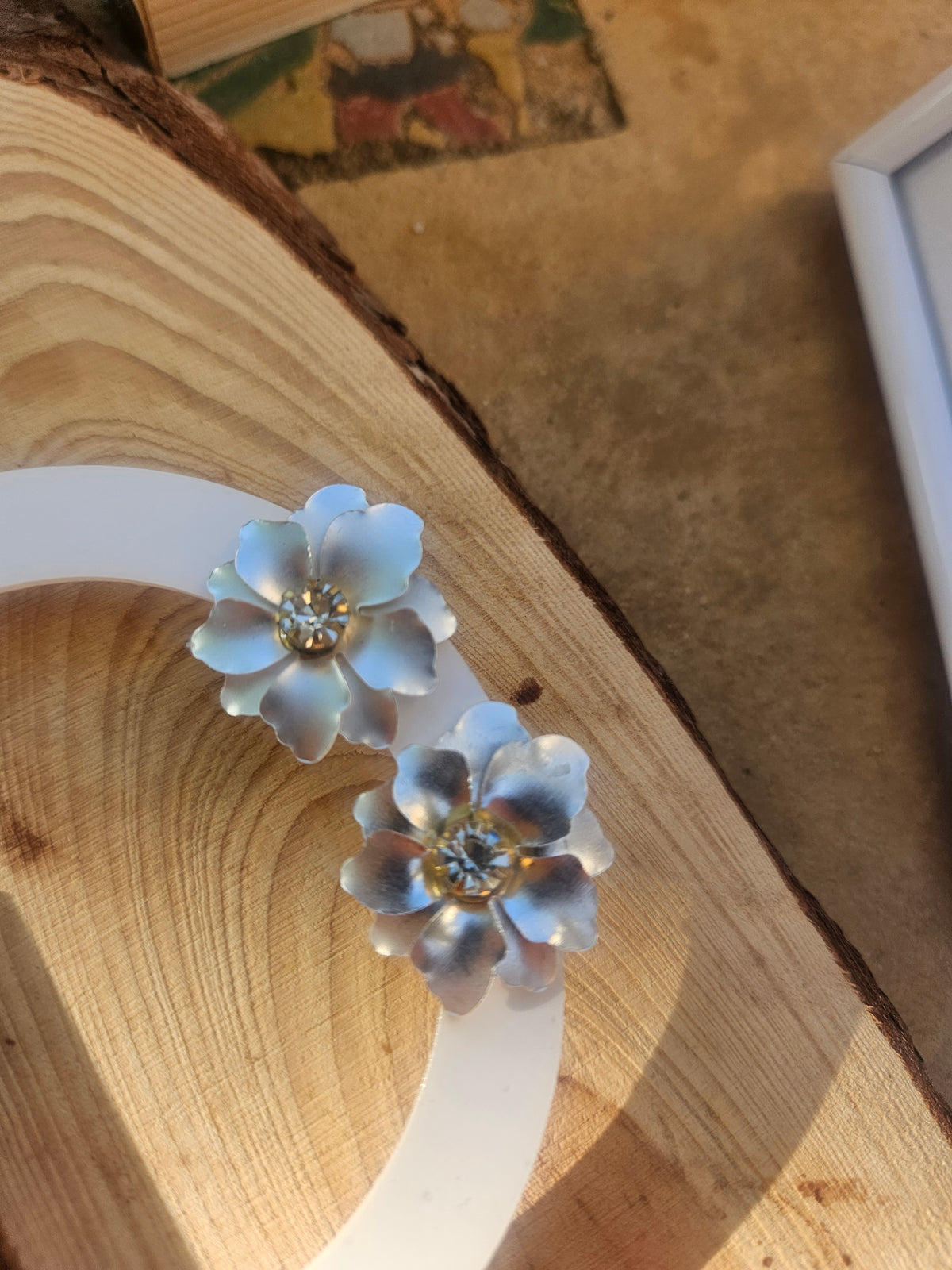 Pendientes de dos flores azul claro con centro dorado, sobre soporte blanco.
