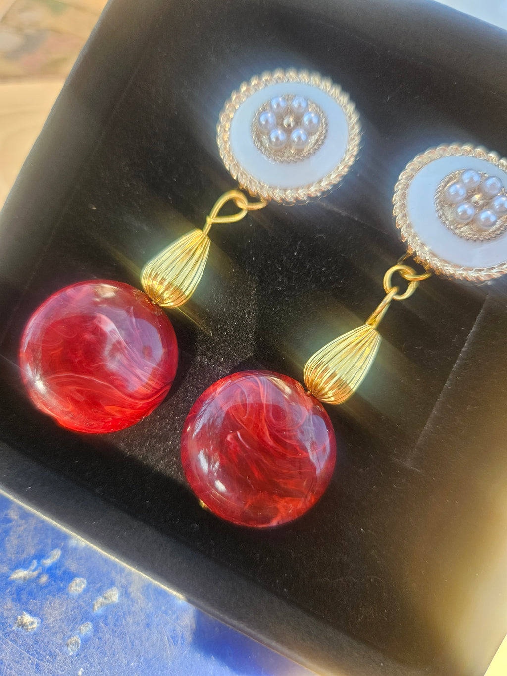 Pendientes dorados con círculos ornamentados y borlas, con cuentas rojas brillantes.