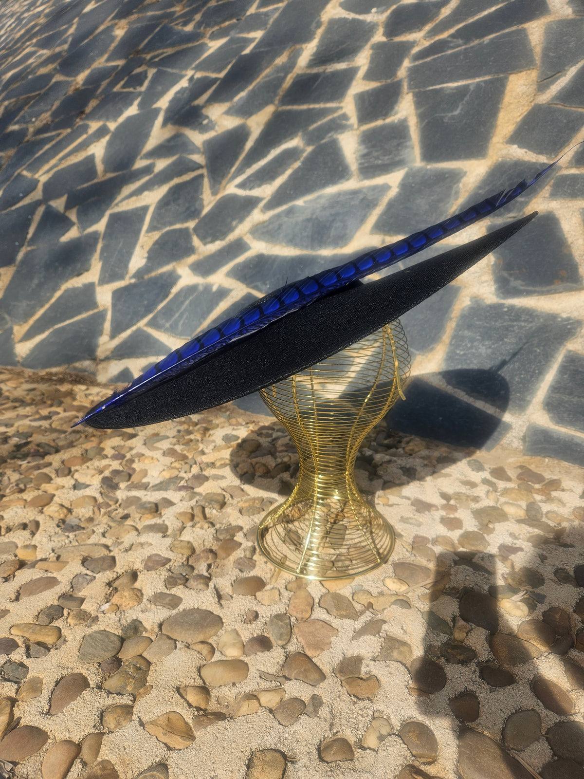 Sombrero negro de ala ancha con pluma azul rayada y cinta delgada sobre el cuerpo