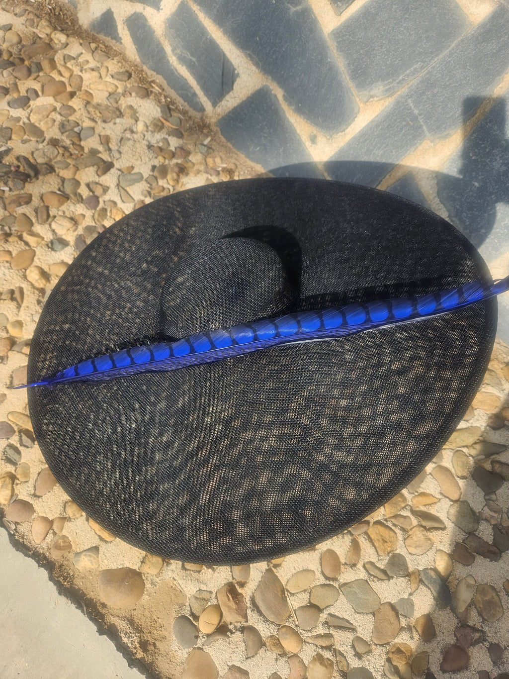 Sombrero negro redondo con franja azul y pluma decorativa en el centro