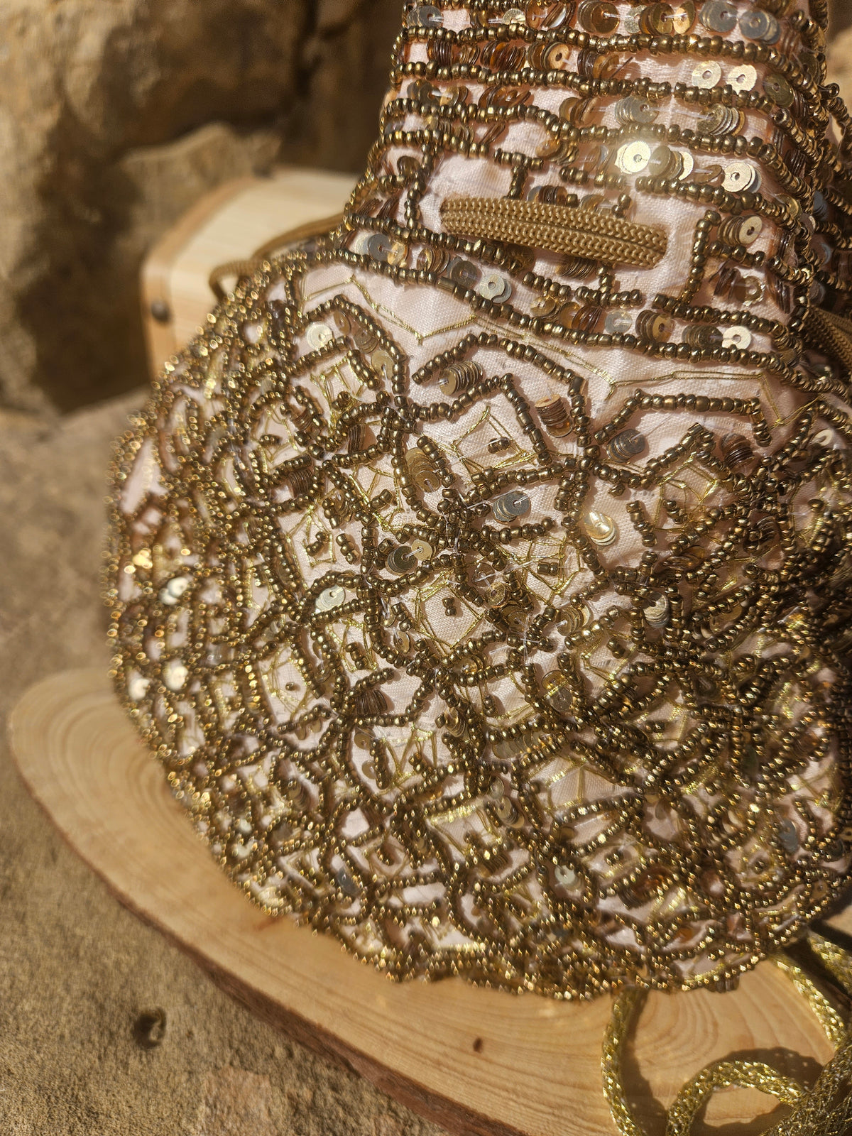 Bolso saco bordado con cuentas doradas y tiras decorativas, con cordón y pompones