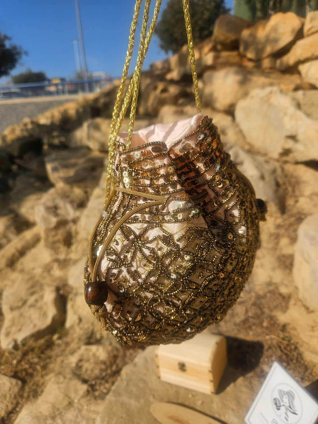 Bolso saco con bordado de cuentas doradas y detalle en espiral, cordones colgantes