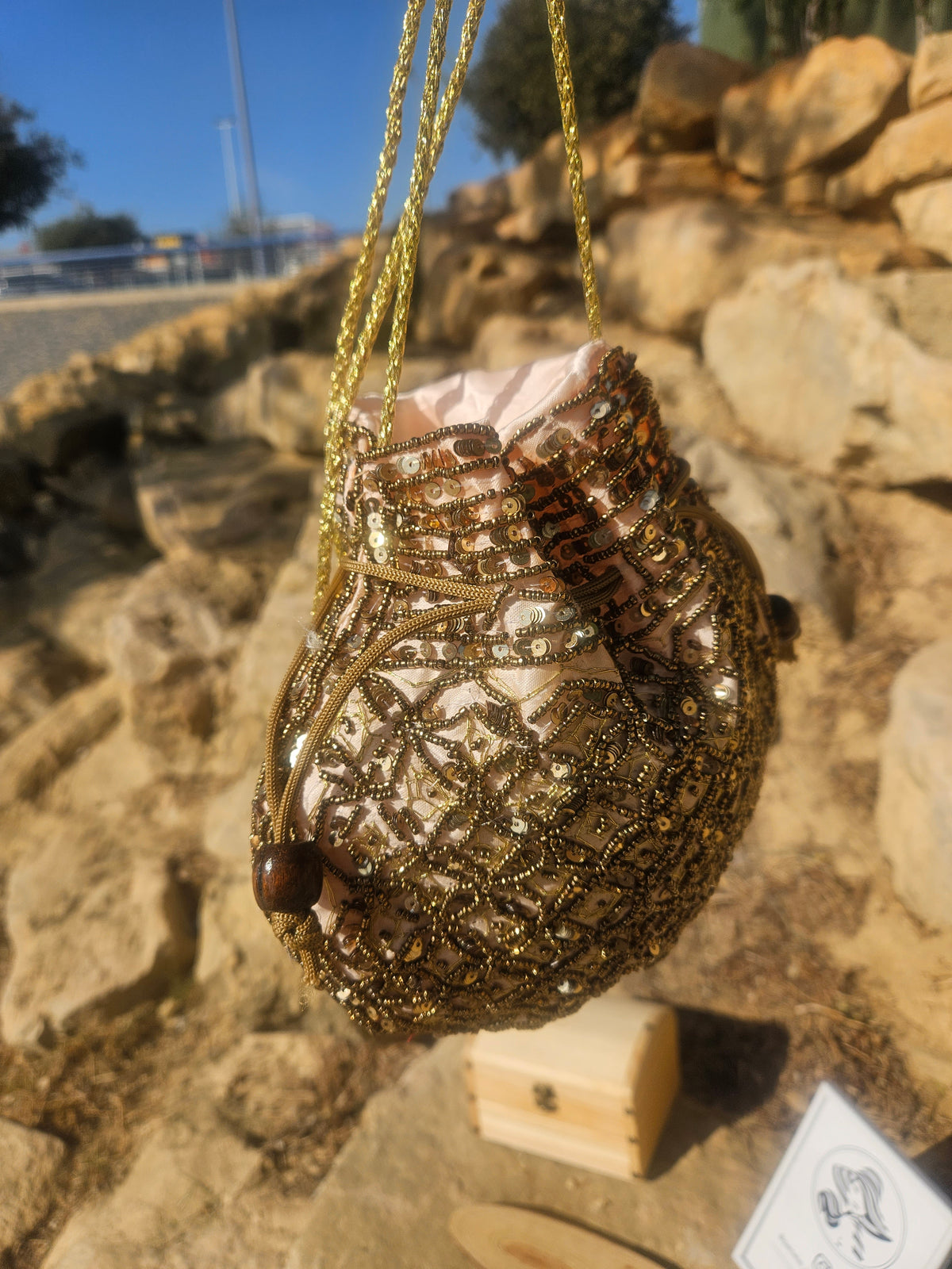 Bolso saco con bordado de cuentas doradas y detalle en espiral, cordones colgantes