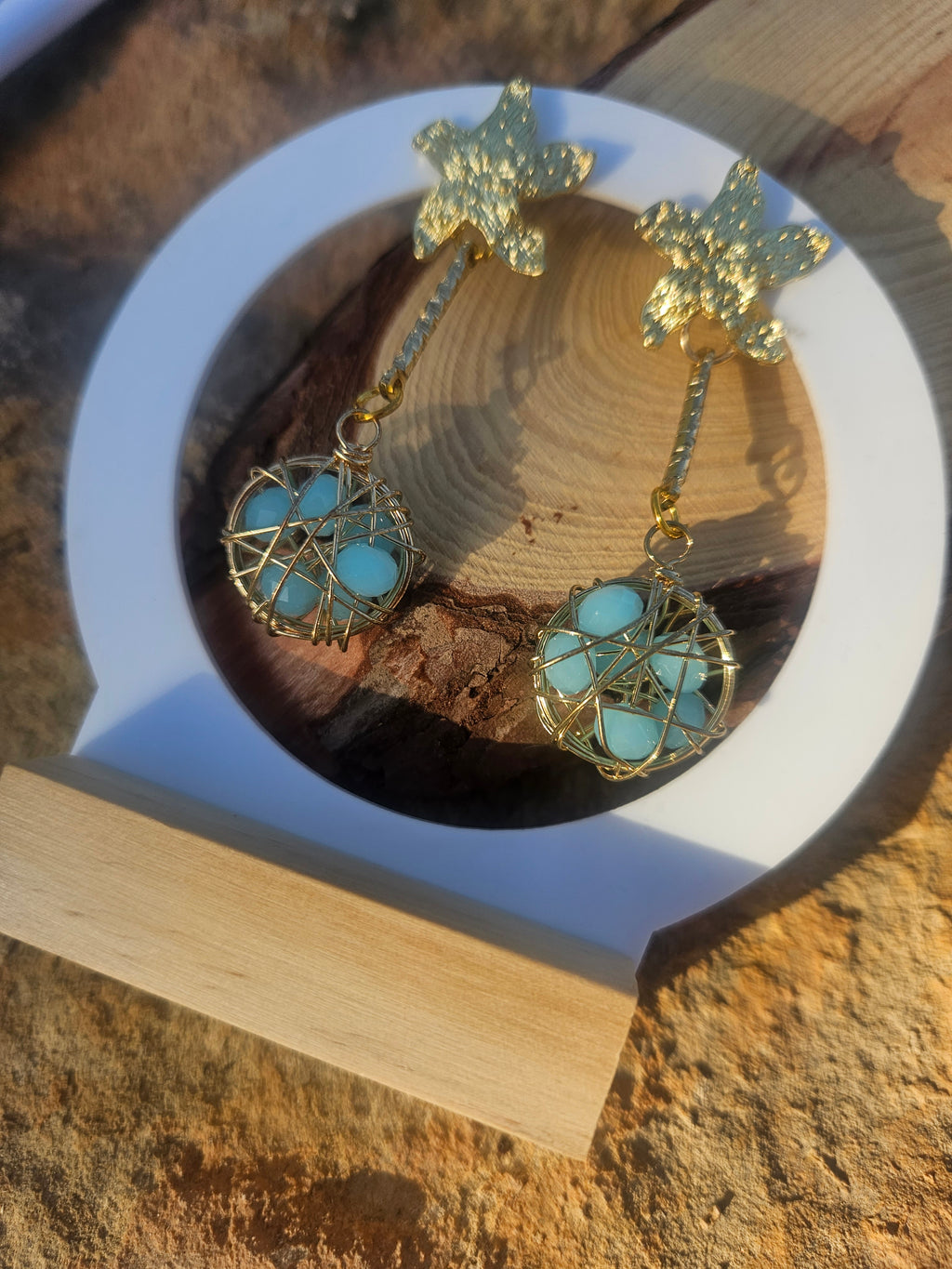Pendientes Caspio dorados con dijes florales y esferas azules enrejadas en vista frontal