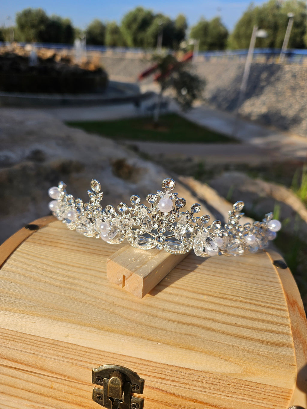 Corona de novia Fátima plateada con pedrería y perlas, vista frontal sobre base de madera