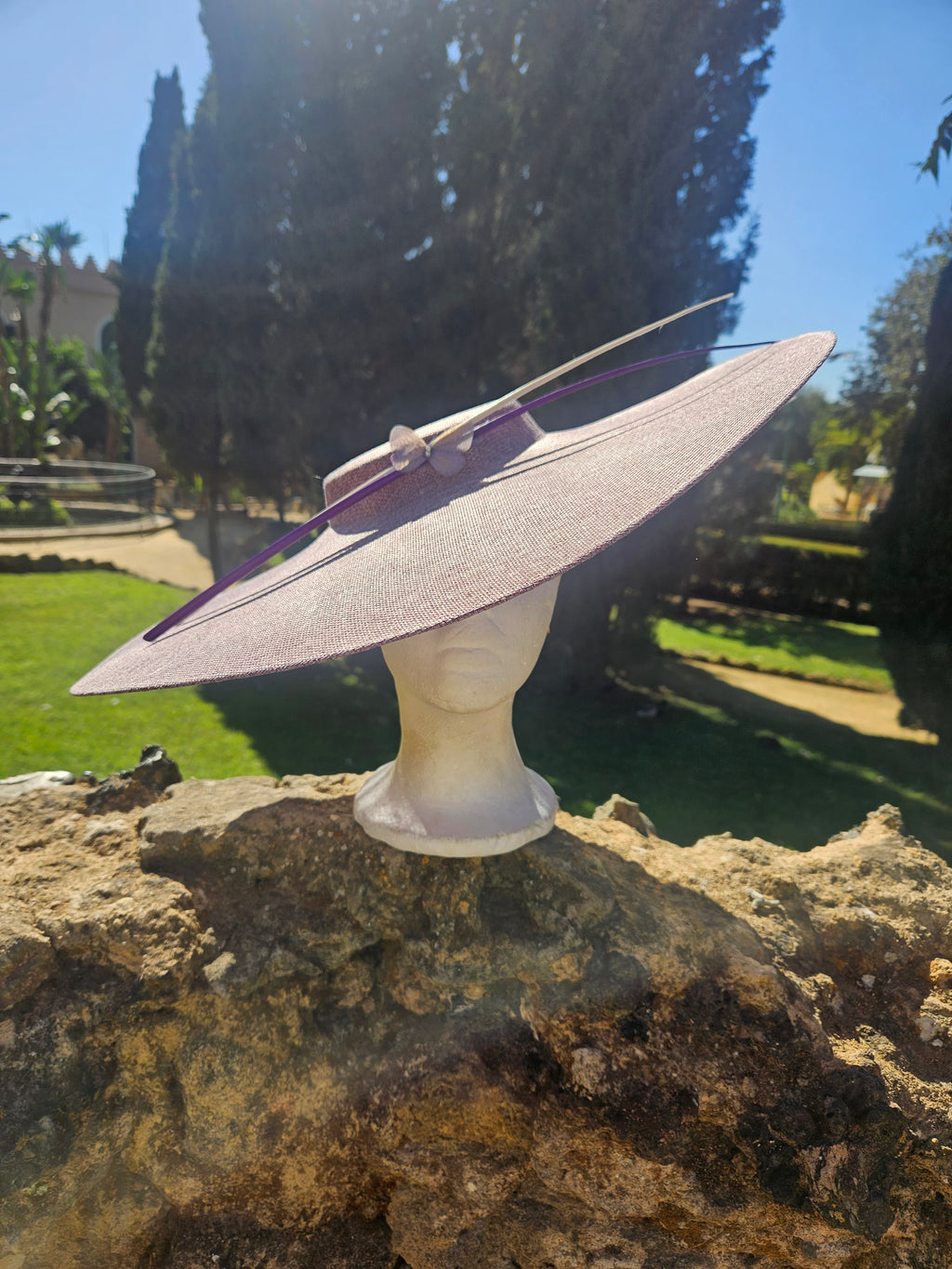 Sombrero pamela rosa claro de ala ancha, con cinta morada y lazo decorativo en la copa.