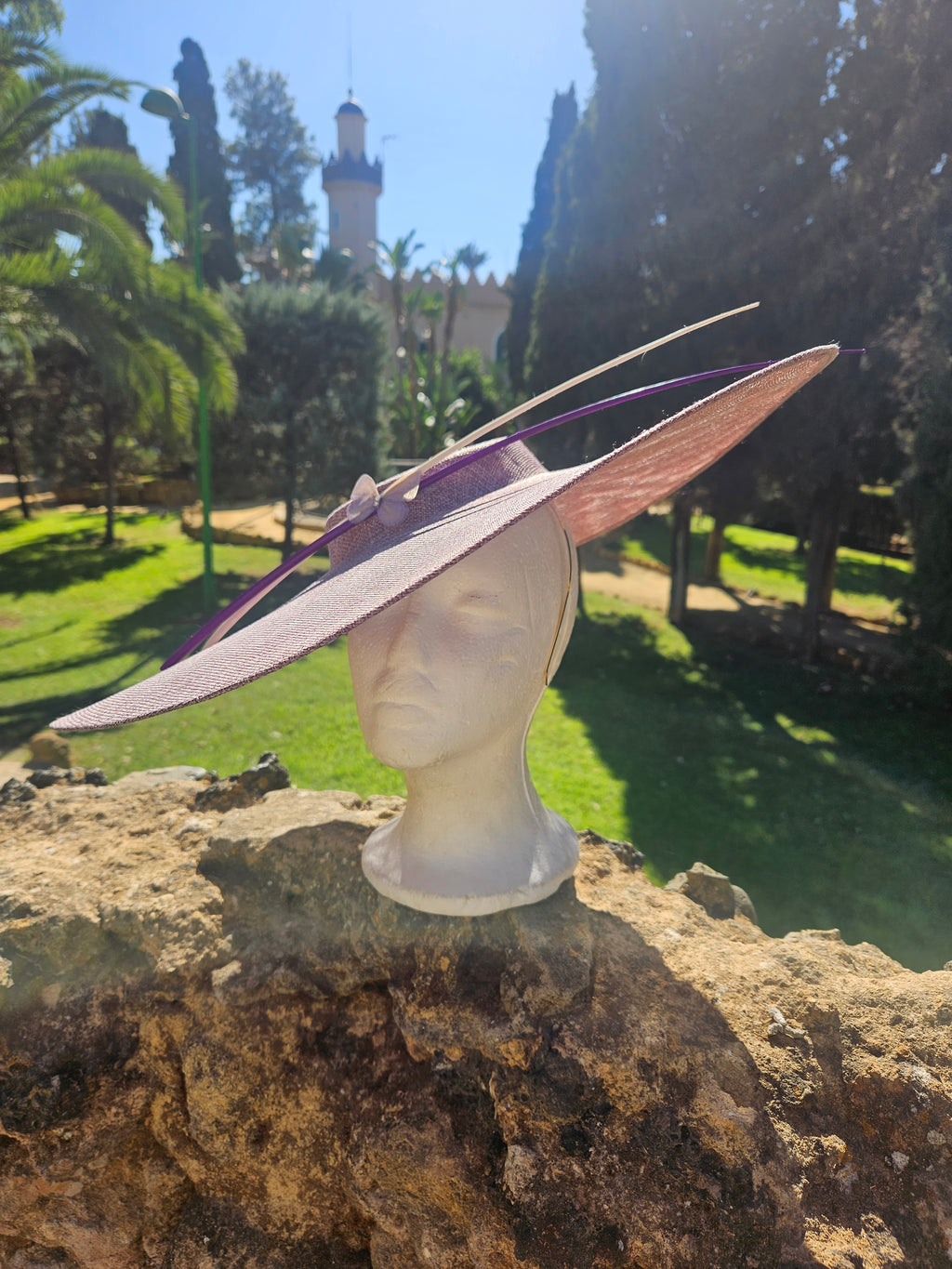 Sombrero pamela con ala ancha rosa claro y cinta morada; diseño con detalle de lazo.