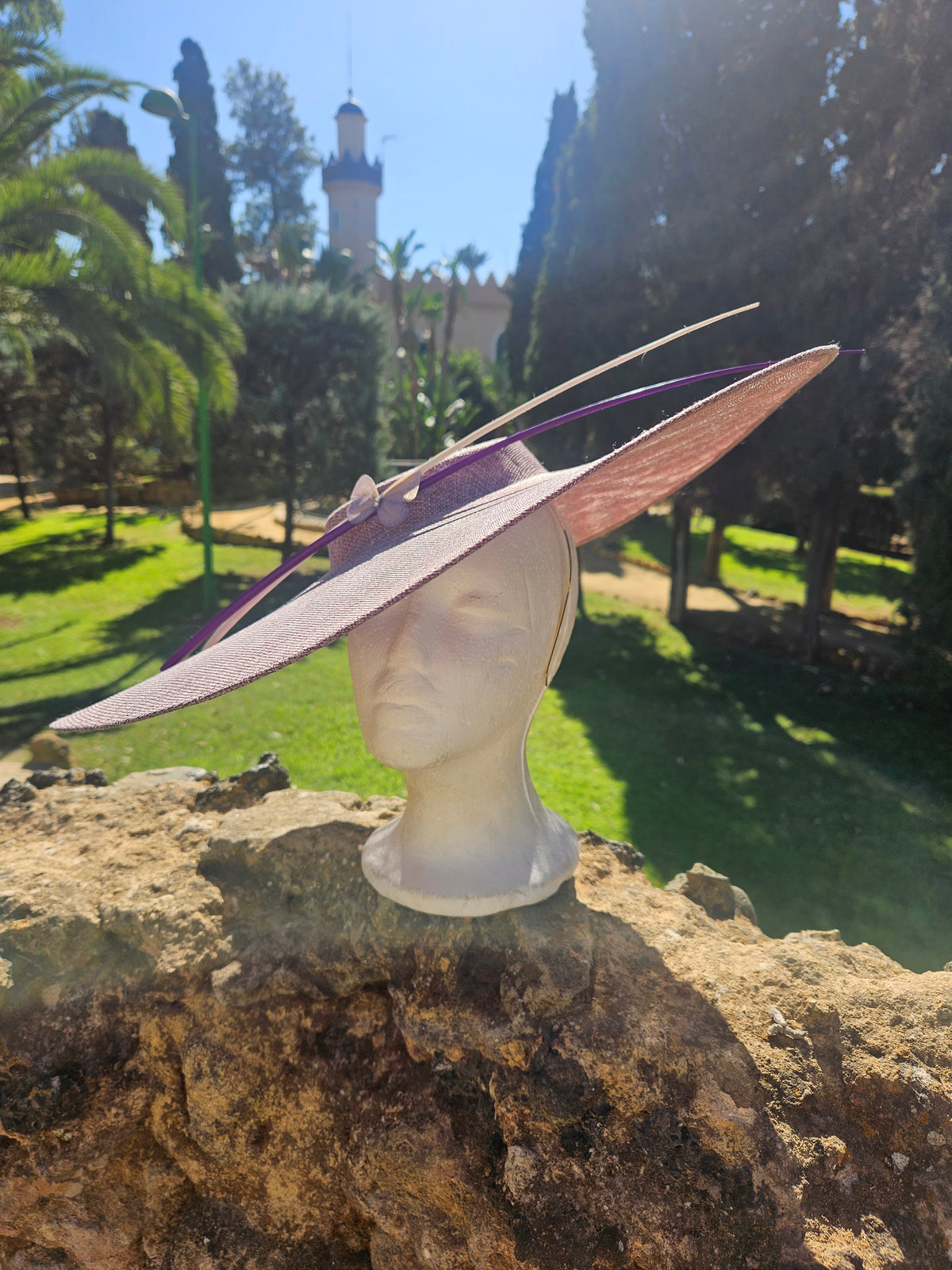 Sombrero pamela con ala ancha rosa claro y cinta morada; diseño con detalle de lazo.