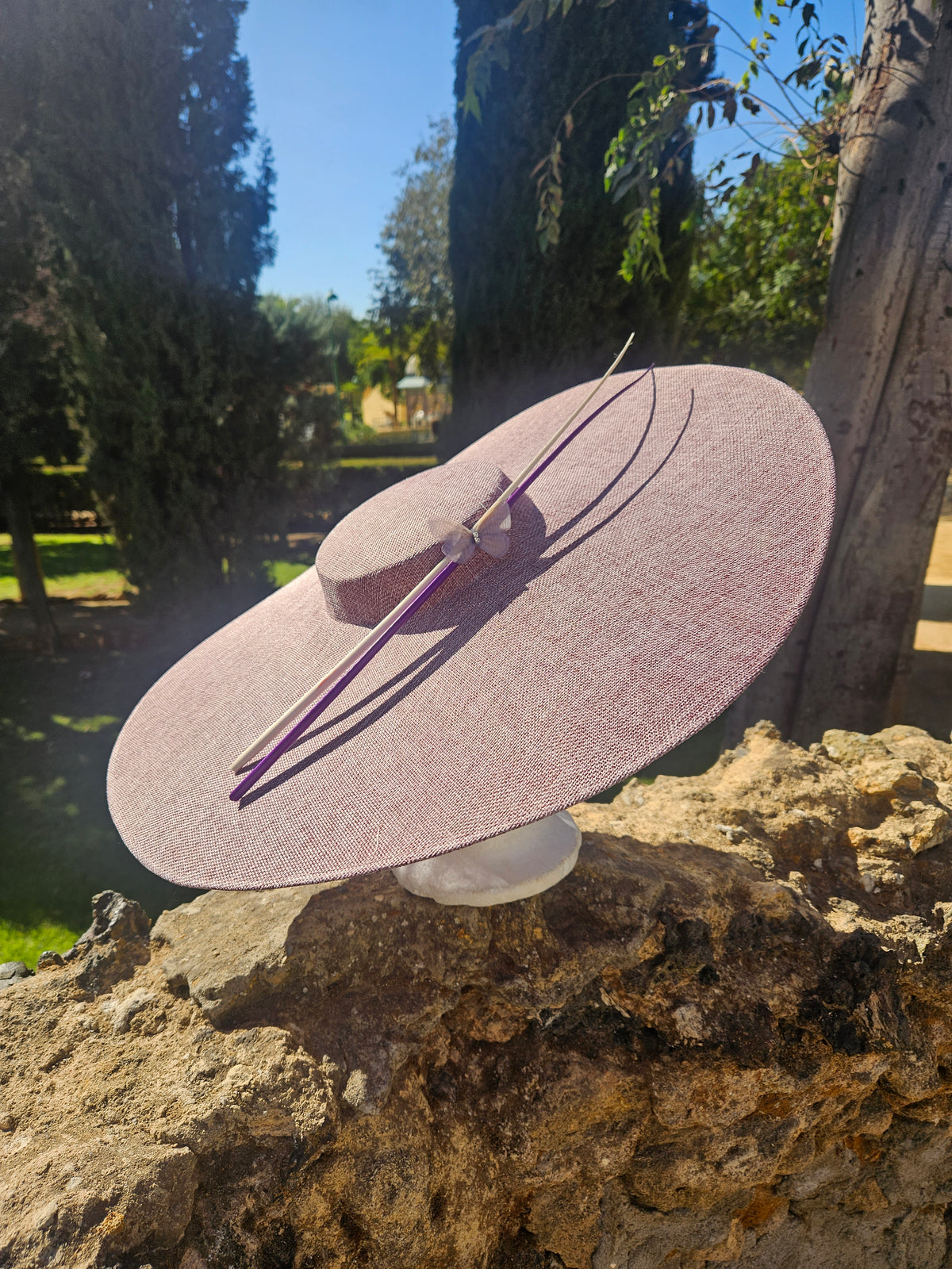 Sombrero pamela rosa con ala ancha y cinta morada cruzada, decorado con lazo en el centro.