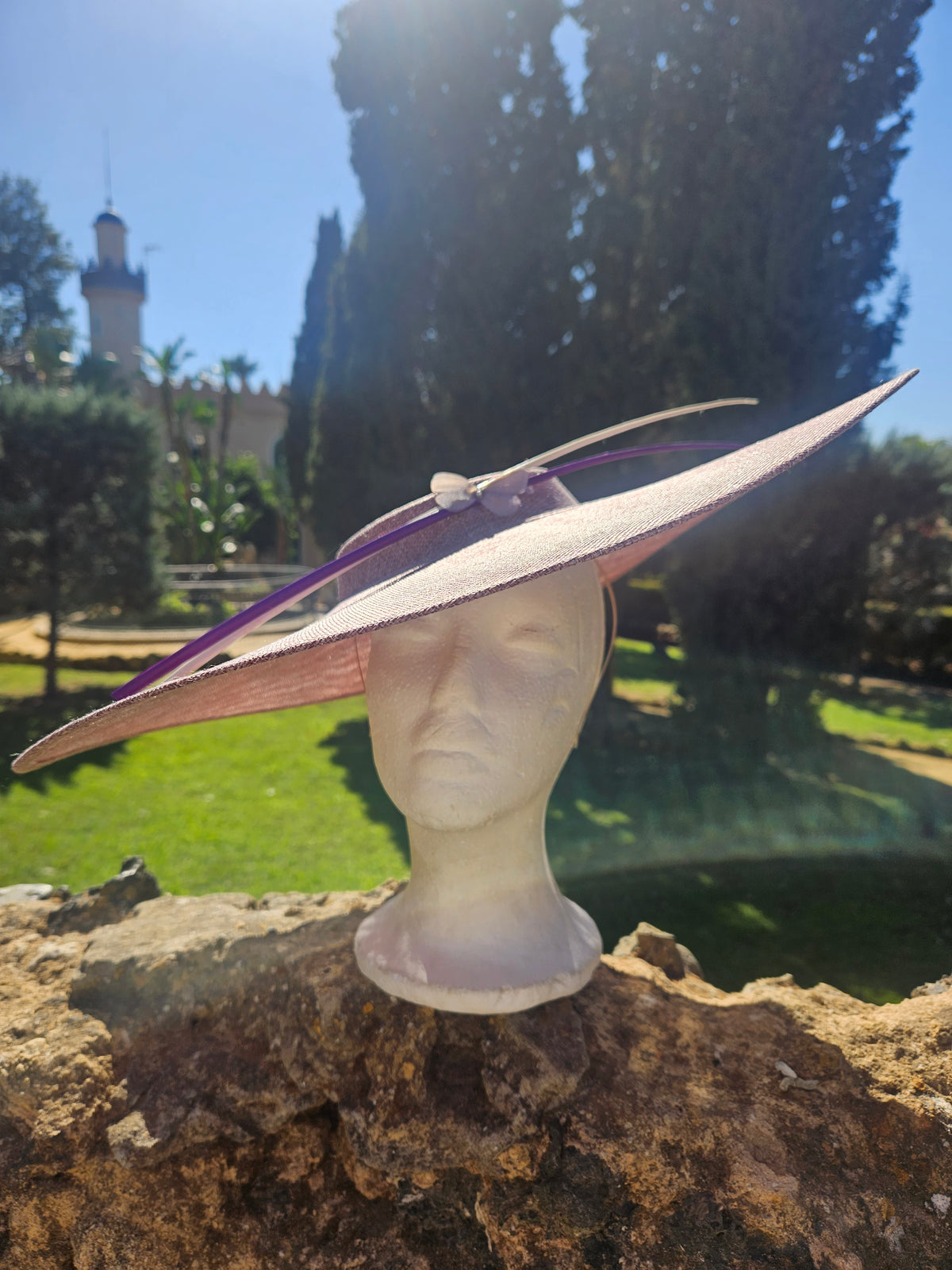 Sombrero pamela rosa claro de ala ancha y cinta morada; vista lateral sobre maniquí.