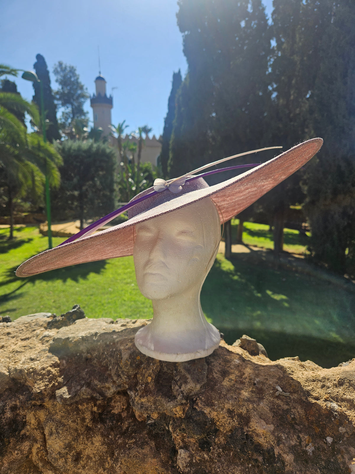 Sombrero pamela rosa claro con ala ancha; borde con tono marrón y cinta morada visible.