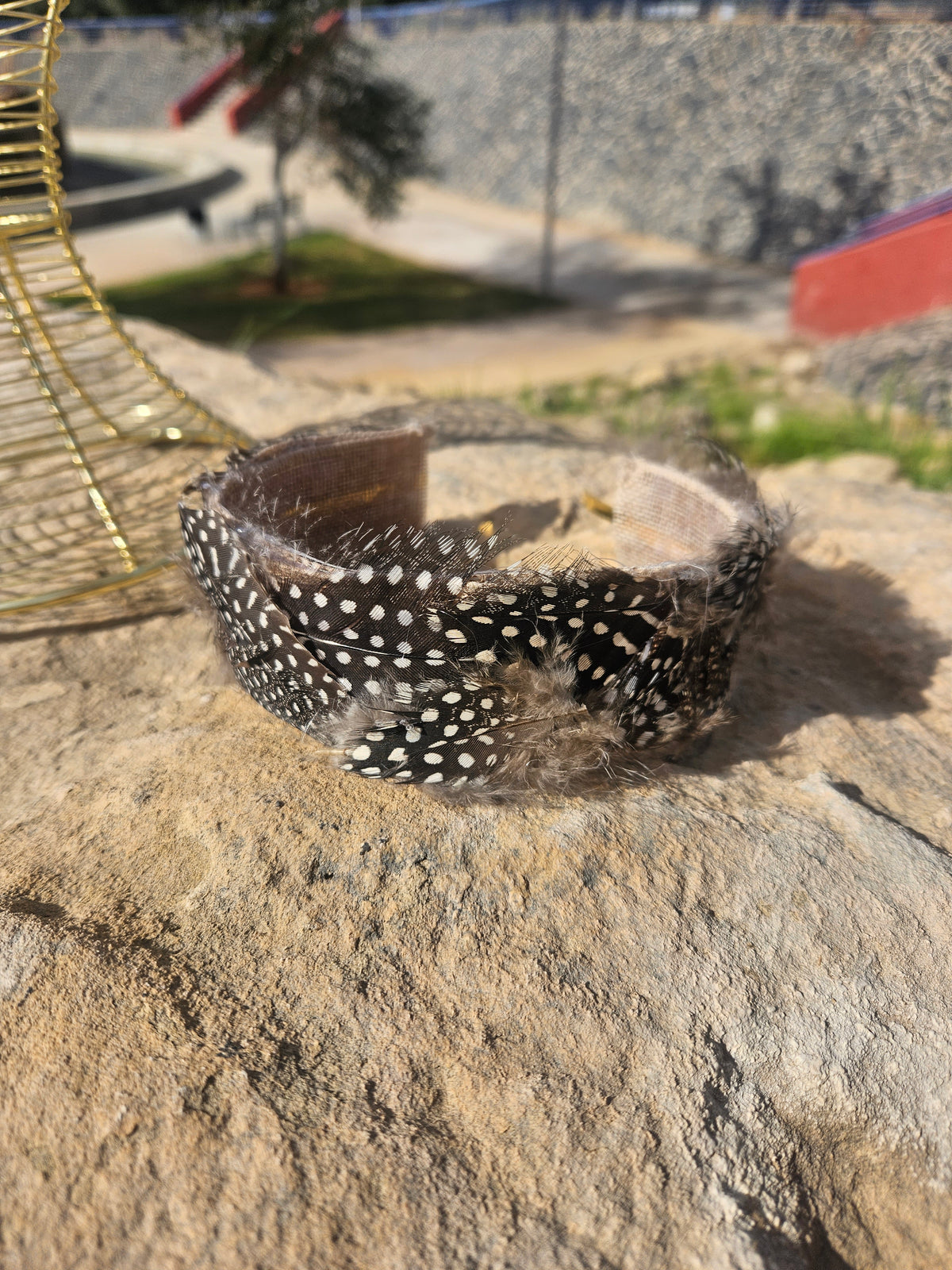 Diadema de malla dorada con banda negra de plumas colocada sobre piedra