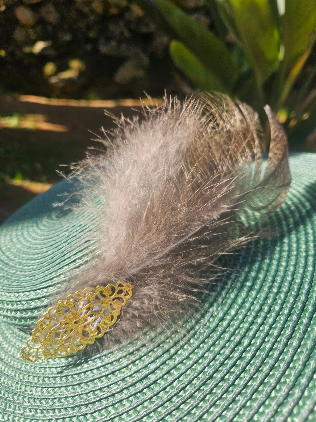 Sombrero turquesa con pluma gris y adorno dorado en la cinta de paja