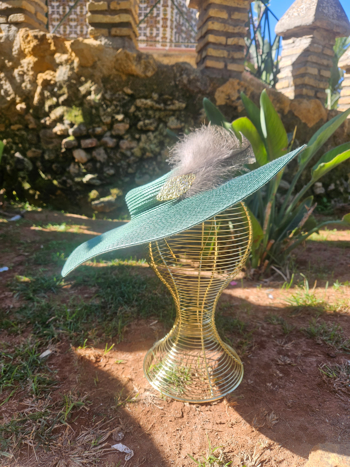 Sombrero de ala ancha turquesa con pluma gris y adorno dorado, vista lateral