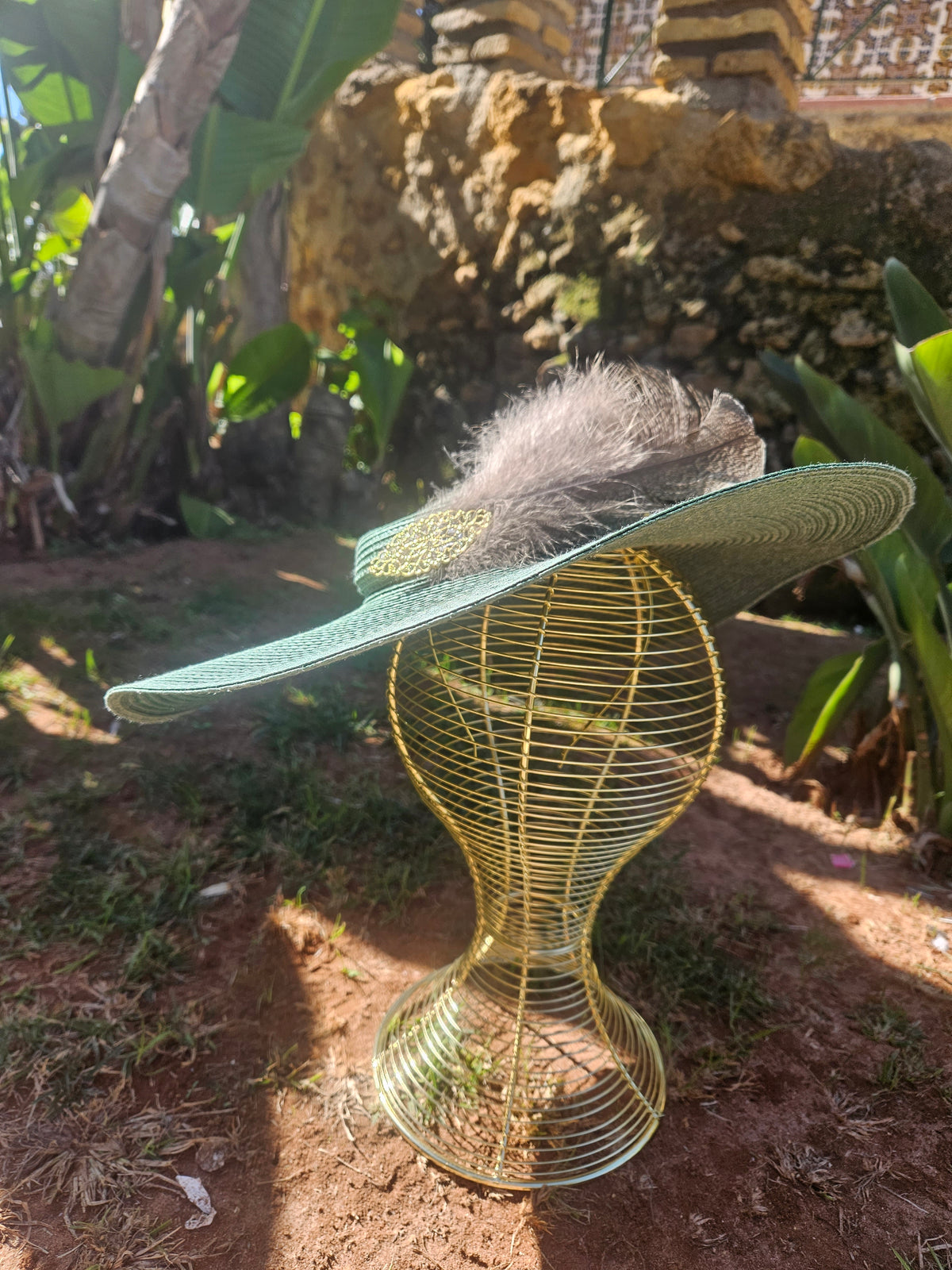 Sombrero de ala ancha turquesa con pluma gris, cinta trenzada y adorno dorado