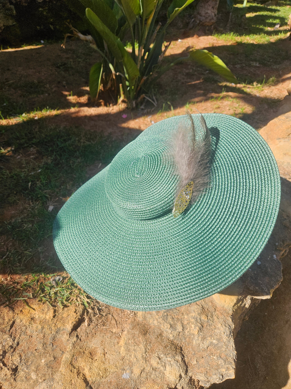 Sombrero de ala ancha turquesa con pluma gris y adorno dorado central, frontal