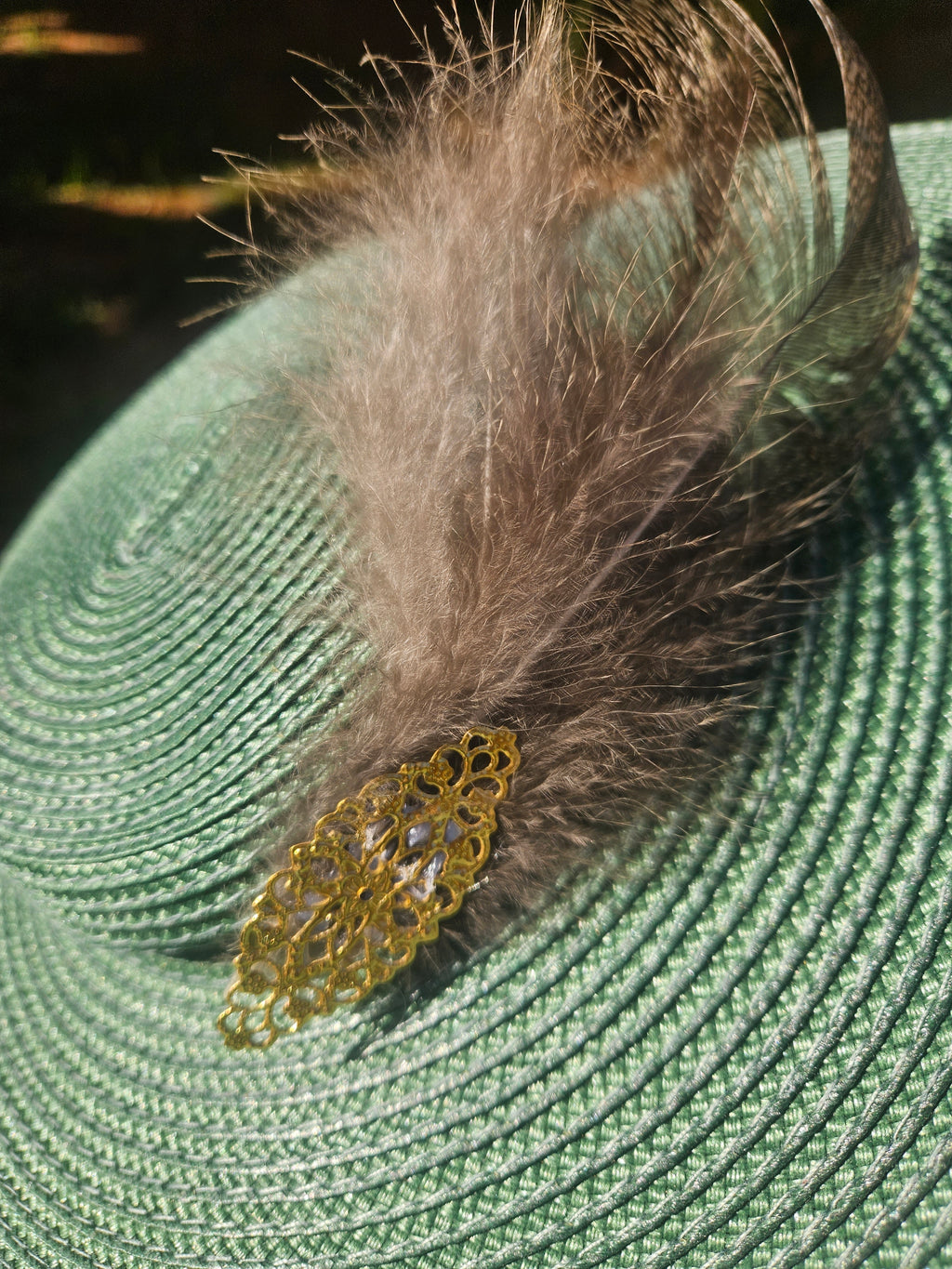 Sombrero turquesa con pluma gris y broche dorado de encaje en la cinta