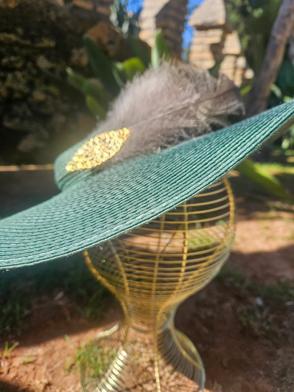 Sombrero turquesa de ala ancha con pluma gris y adorno dorado, vista en ángulo