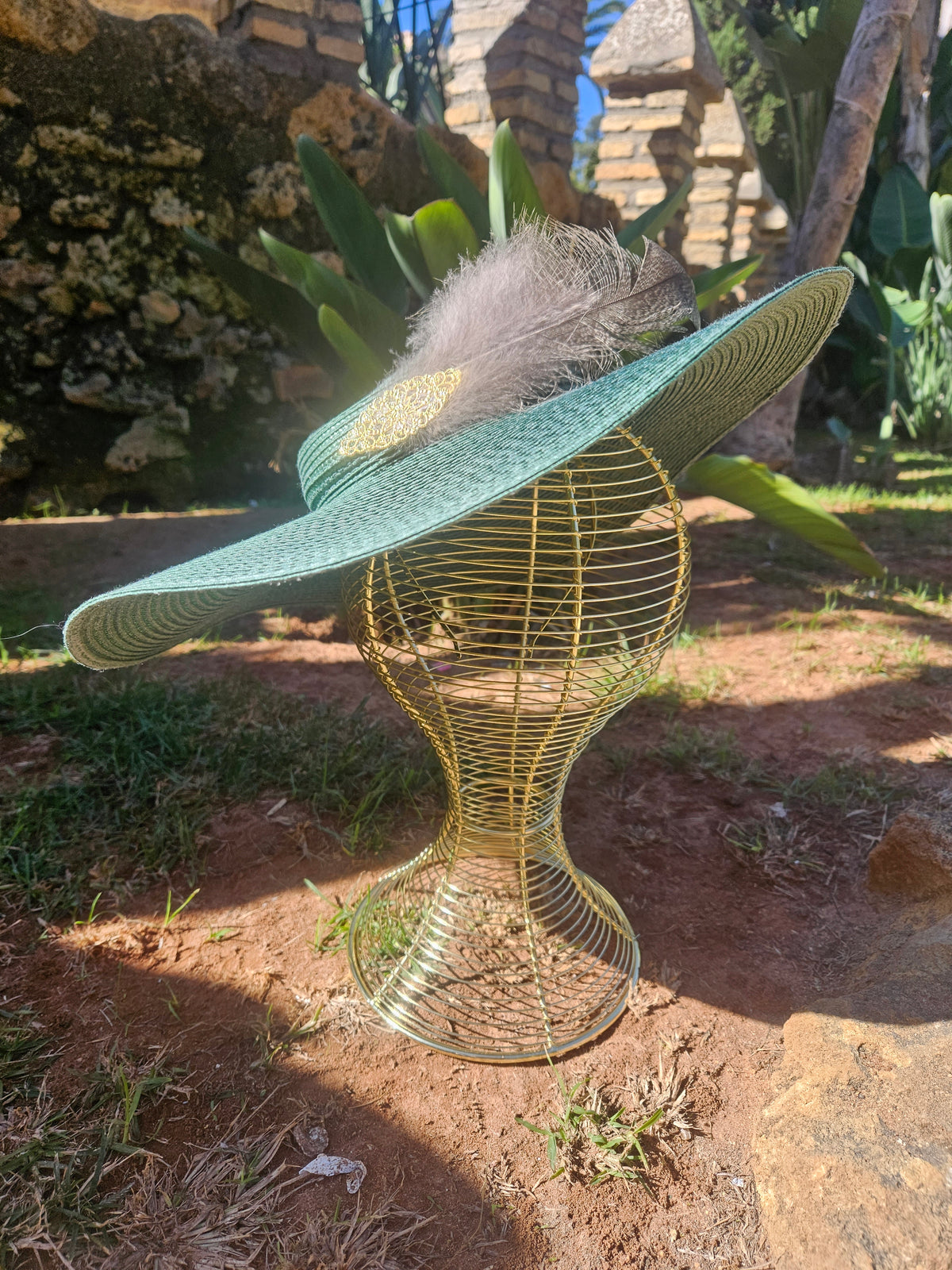Sombrero turquesa de ala ancha con pluma gris y adorno dorado, vista completa