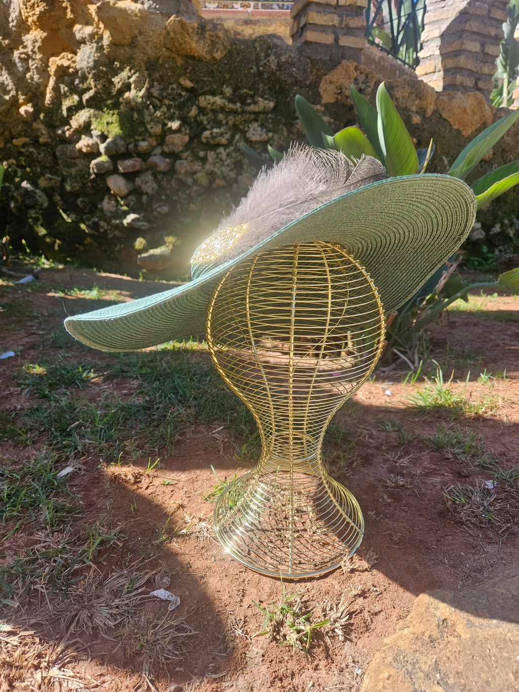 Sombrero turquesa de ala ancha con pluma gris y adorno dorado, pose inclinada