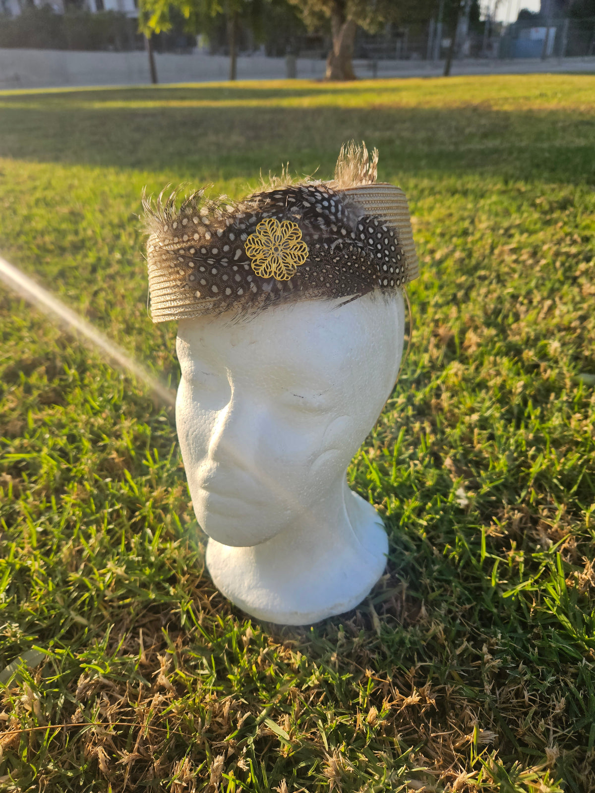 Sombrero casquete beige con ala corta y malla negra punteada, plumas y flor bordada