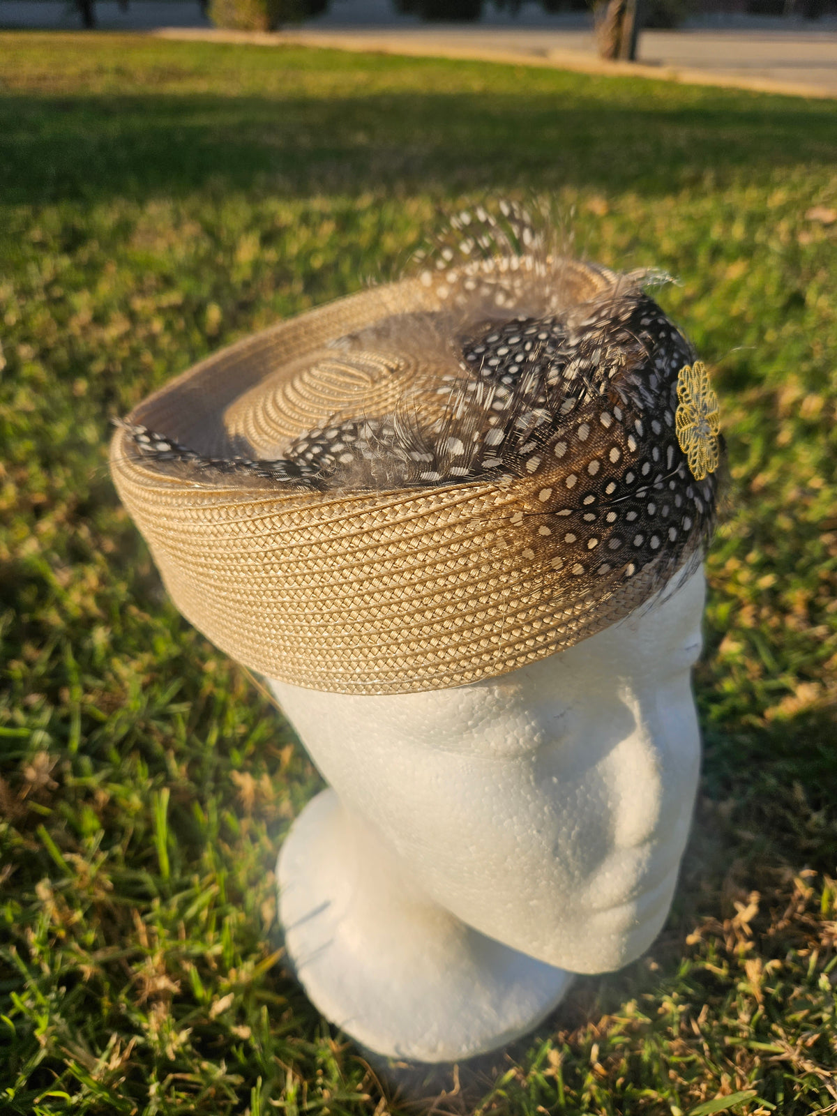 Sombrero casquete beige con malla negra punteada, plumas laterales y flor amarilla bordada