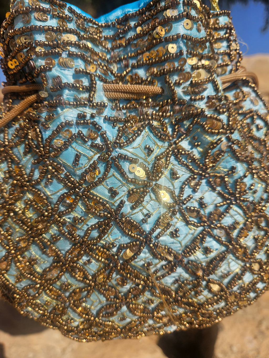 Bolso de saco turquesa con bordado de lentejuelas doradas y patrón geométrico.