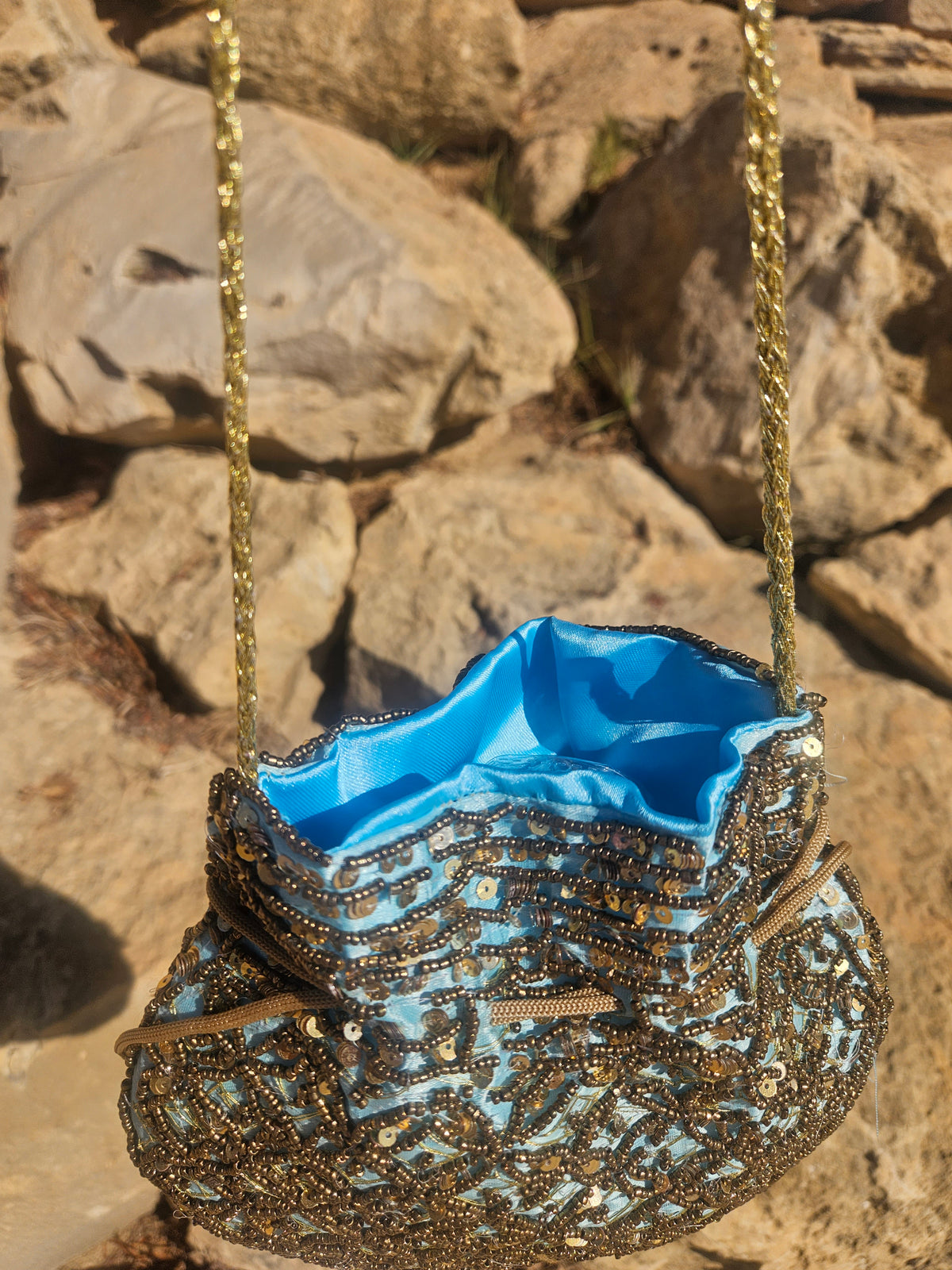 Bolso de saco con forro turquesa y cuentas doradas, asa de cadena trenzada.