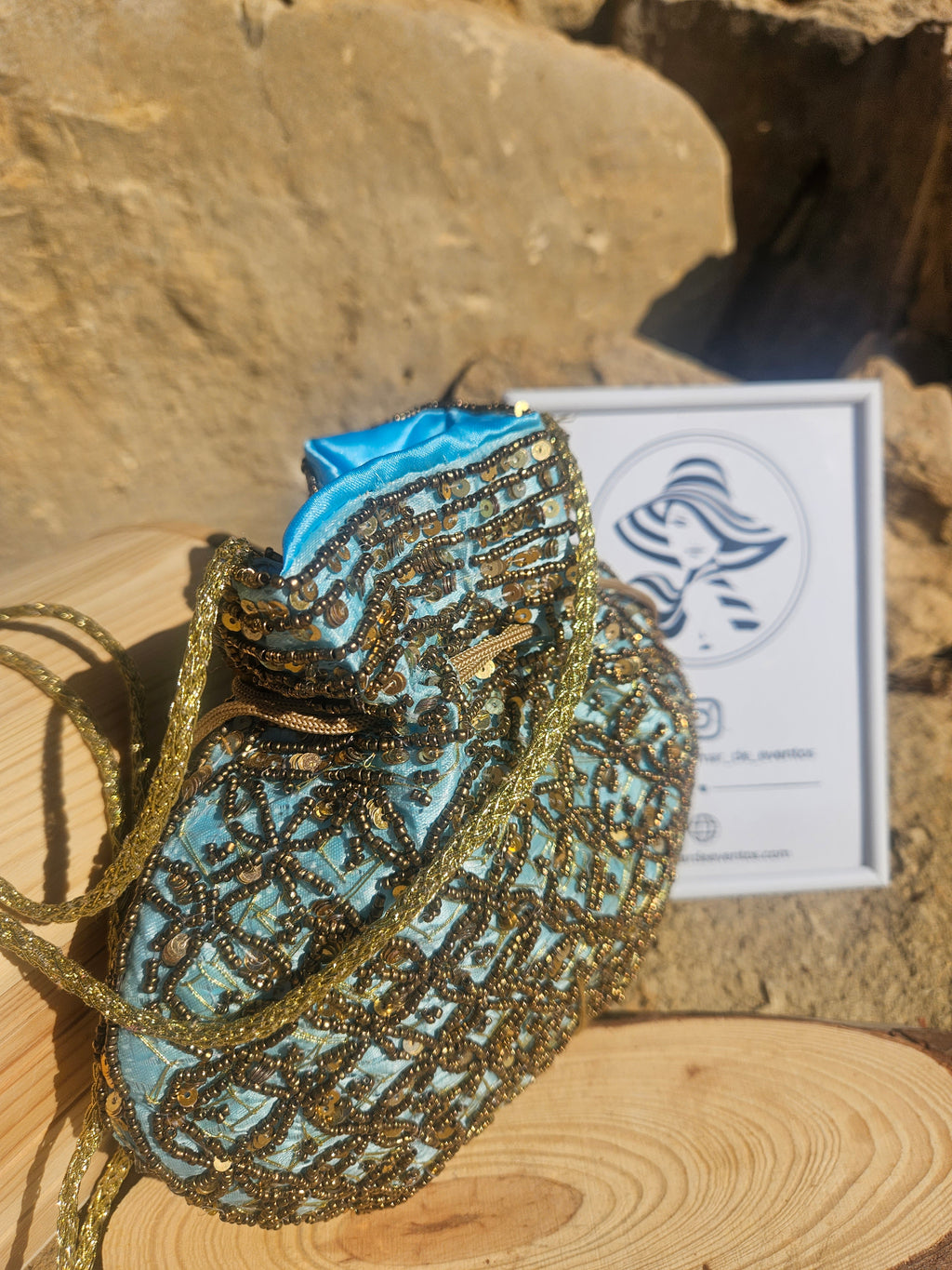 Bolso de saco con forro turquesa, bordado dorado y asa de cadena trenzada.