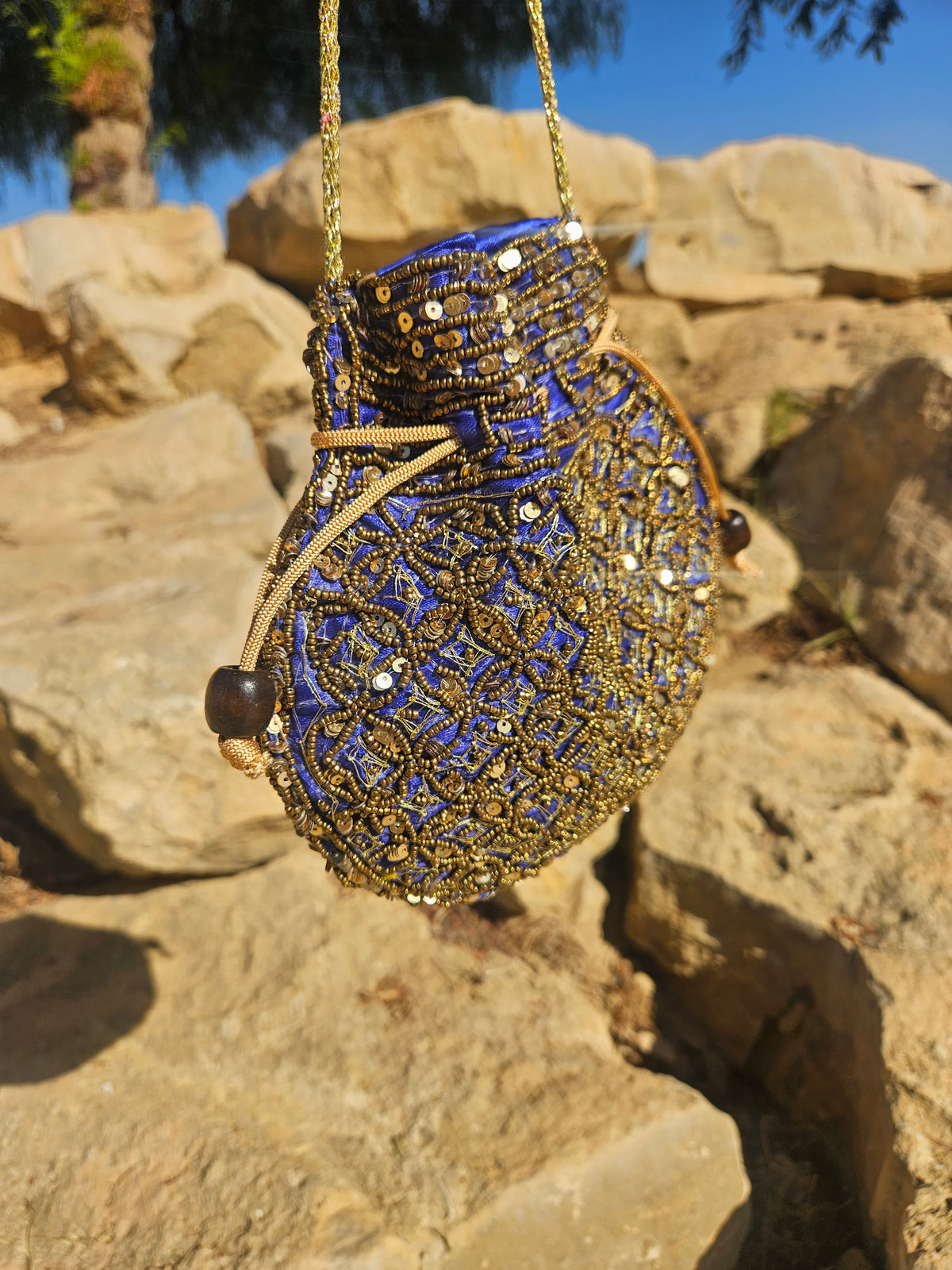 Bolso redondo azul y dorado con bordado detallado, asa de cadena y tiras