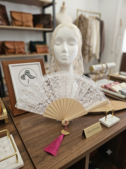 Abanico de encaje blanco con varillas de madera y borla fucsia en mesa de tienda