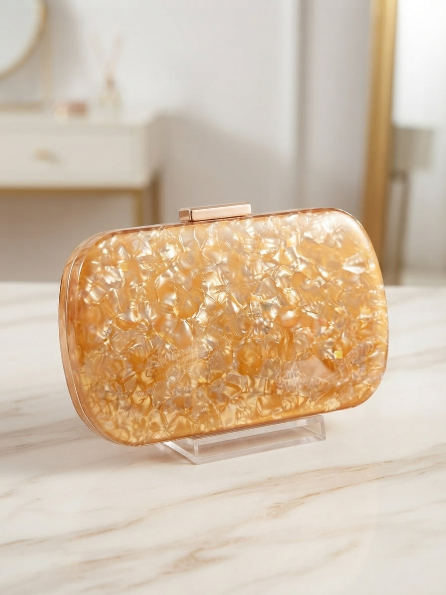 Bolso tipo clutch ámbar con cierre metálico y textura brillante, sobre soporte acrílico