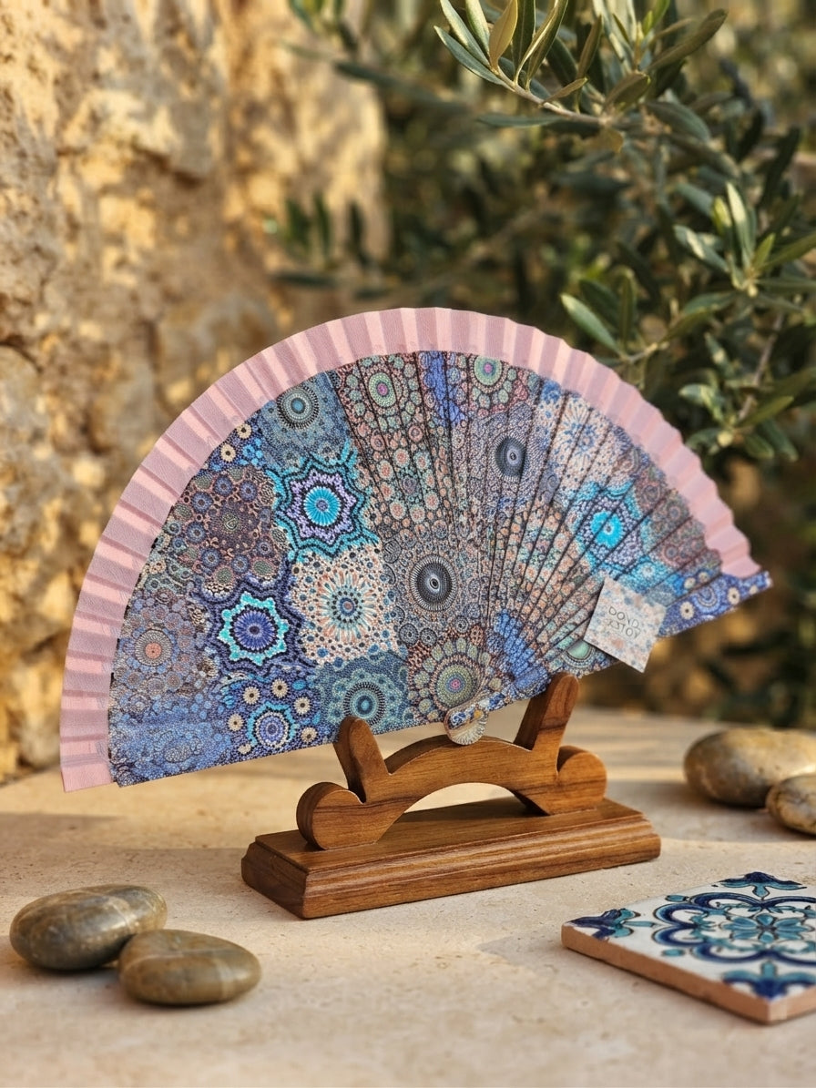 Abanico geométrico rosa abierto sobre base de madera, patrón mandala azul