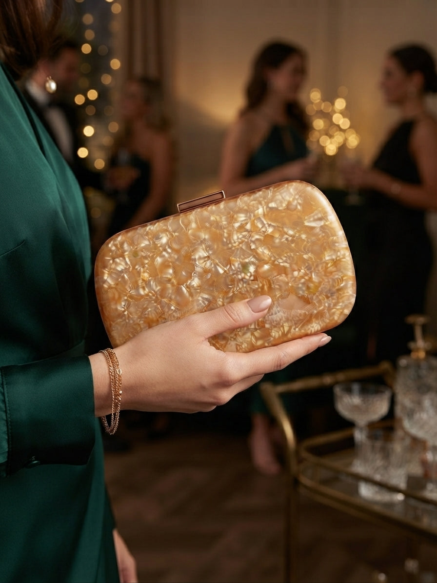Bolso clutch ámbar con cierre metálico, sostenido en la mano con textura brillante