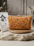 Bolso de cuentas naranja multicolor con asa metálica, sobre soporte redondo.
