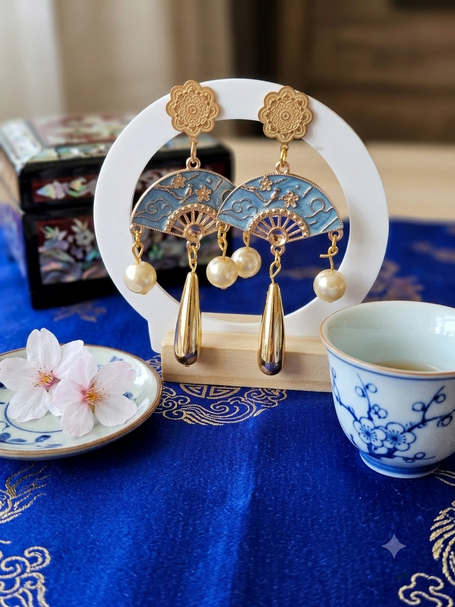 Pendientes azules con abanico dorado, borlas y perlas; cierre superior floral dorado.
