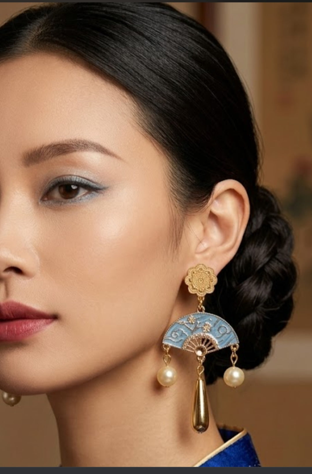 Pendiente dorado con aro azul y perlas colgantes; pieza superior floral sobre oreja.